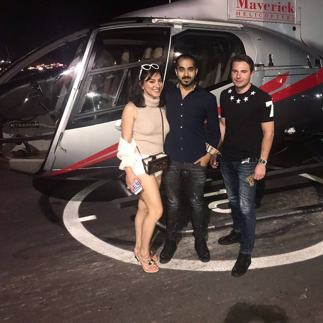 Three individuals pose in front of a helicopter at night.